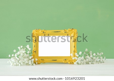 Image of beautiful bouquet of spring flowers next to blank vintage photo frame on wooden table. For photography mock up montage