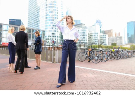 Blonde secretary looking at camera and playing with hair near talking employees background. Concept of businessperson and La Defense Paris. Young blonde woman is beautiful.