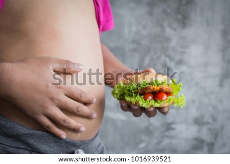 Close up stomach of fat boy enjoy eating with hamburger, concept healthy and lose weight ,selective and soft focus
