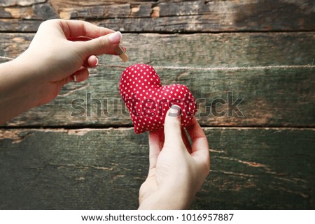 Female hands hanging red heart on rope on wooden background