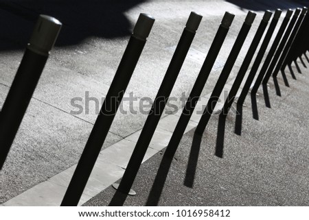 Close up view of a row of iron vertical tubes placed on a sidewalk bordure. Urban picture with shadows of tne metallic elements on the floor. Geometric and graphic composition during a sunny day. 