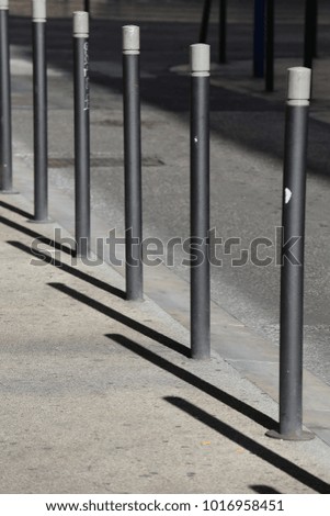 Close up view of a row of iron vertical tubes placed on a sidewalk bordure. Urban picture with shadows of tne metallic elements on the floor. Geometric and graphic composition during a sunny day. 