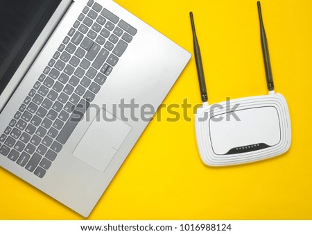 A laptop and a wi-fi router on a yellow paper background. Keyboard, touchpad. Modern digital technologies. Copy space. Top view.