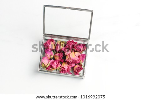 buds of roses in a glass box on a marble table. pink dried flowers. creative layout, minimal concept, flat lay
