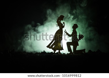 Will you marry me? Silhouette of young man staying on the knee and making proposal for his lovely girl against dark toned background. Valentine greeting card decor. Selective focus