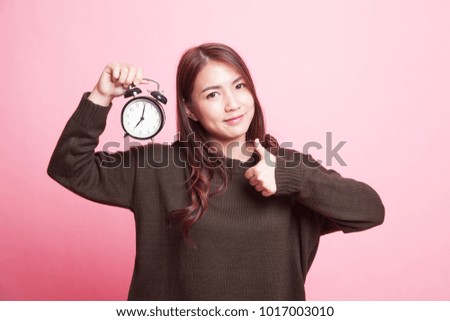 Young Asian woman show thumbs up with a clock on pink background