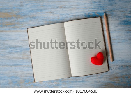 Red heart on book with pencil on blue background, Valentine concept.
