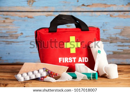Healthcare concept with First Aid kit with pills, syringe, bandages and thermometer spread out in front of it on rustic wood