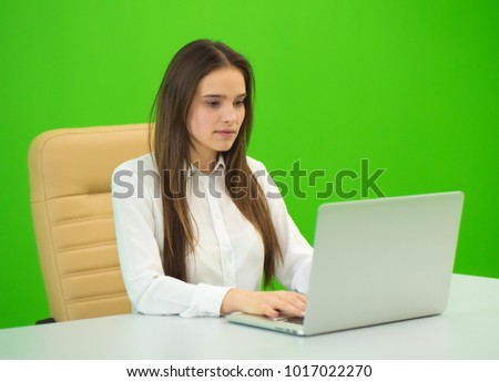 The woman sit near the laptop on the green background