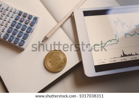 Close up view a bitcoin gold, a stock graph on a tablet screen and blank note with calculator