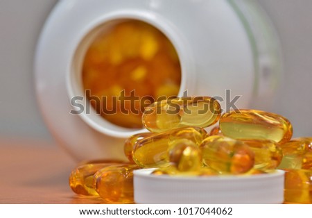 Yellow supplement capsules spilled over a lid with the overturned bottle in the background, with more pills visible inside.