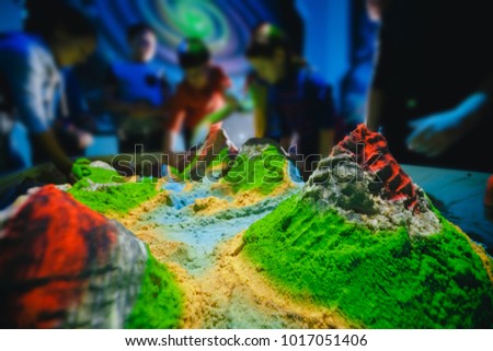 Kinetic sand, hands of children erect volcanoes, hills, rivers, play in simulator of earth, soil.