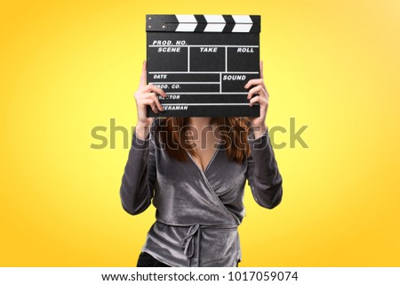 Beautiful young girl holding a clapperboard on colorful background