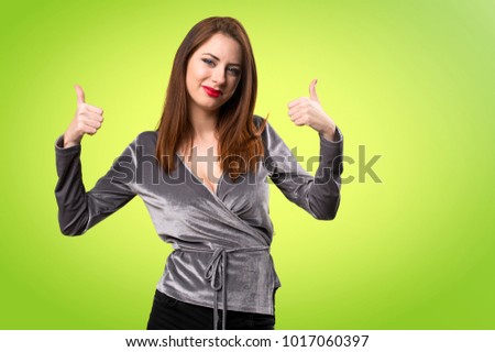 Beautiful young girl with thumb up on colorful background