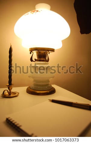 Lamp, candle stand on the table, next is a notebook with a pen