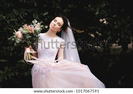 Portrait of the bride in the forest. Bride in a pink dress with a bouquet of flowers and greens.