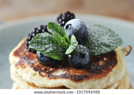 Pancakes on a blue plate. Pancakes are decorated with blueberries, blackberries, mint. The dish is sprinkled with powdered sugar. Wooden background. Close-up. Macro photography.