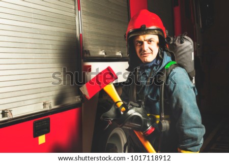 Rescue firefighter man in a fire holds iron axe, on the background of a fire truck