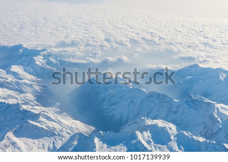 Aerial view of the Swiss alps. Flying over Alps. Amazing view on mountain. Aerial view of misty mountains and clouds above the mountain peaks, blue tinted. 