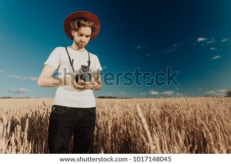 Young handsome guy with medium format film camera, standing on a wheat field. Photographer in creative process at outdoor location.