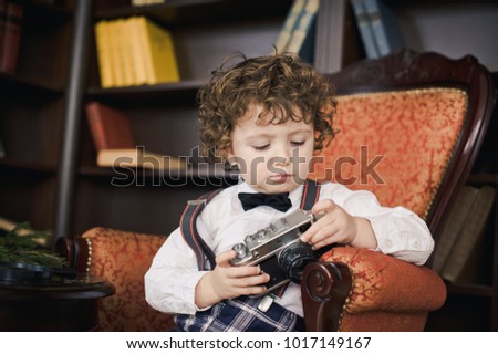 The boy in the armchair in the library. Curly little boy with old camera
