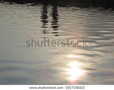 The reflection of the sun in the river, shadows of people in the water 