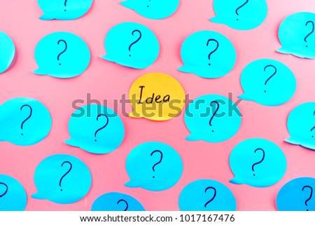 Unusual background with stickers. The word idea written on an orange sticker, among the question marks on turquoise papers.