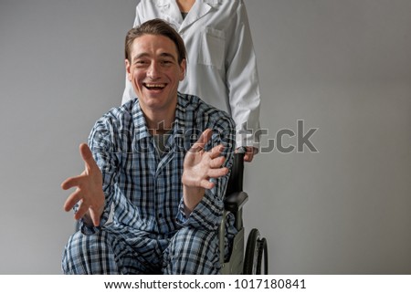 Portrait of happy patient sitting in means for movement of invalids. Medical assistant is standing behind him. Copy space in right side. Isolated on background