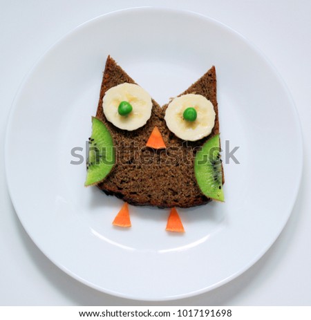 Healthy food art for children. Funny breakfast. Owl from fruit on white plate, top view.