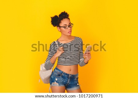 Young african woman isolated on yellow wall studio teen style with knapsack browsing smartphone