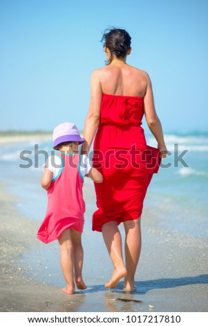 Back view of a mother with her little girl walking on the seasho