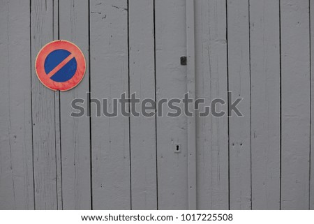 Street view of the sign indicating the interdition to park a car in front of the house garage door. Ban to park. Circular blue and red sign fixed on grey planks of wood. Minimalist urban picture.  