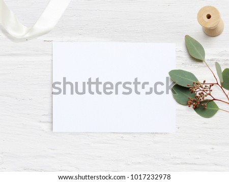 Feminine wedding desktop mock-up with blank paper card and Eucalyptus populus branch on  white shabby table background. Empty space. Styled stock photo, web banner. Flat lay, top view.