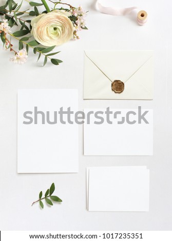Feminine wedding, birthday desktop mock-ups. Blank greeting cards, envelope. Eucalyptus branches, pink cherry tree blossoms and Persian buttercup flowers. White table background. Flat lay, top  view.