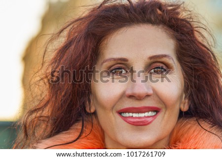 Closeup of a beautiful smiling mature woman with wrinkles and slight strabismus of Venus wearing orange fur collar