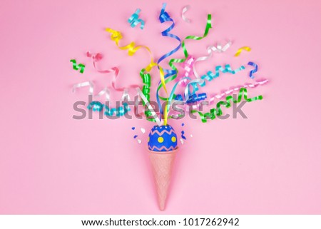 Happy Easter concept. Blue egg in waffle cone with colorful ribbons on center on pink background