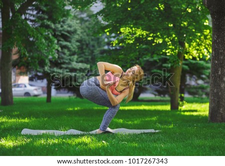 Fitness, woman training yoga in twisting awkward pose outdoors in the park, copy space. Young slim girl makes exercise. Stretching, wellness, calmness, relax, healthy, active lifestyle concept
