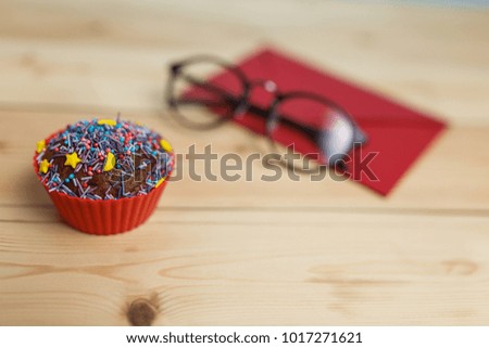 red envelope with a cupcake and glasses on the table, a letter to a loved one