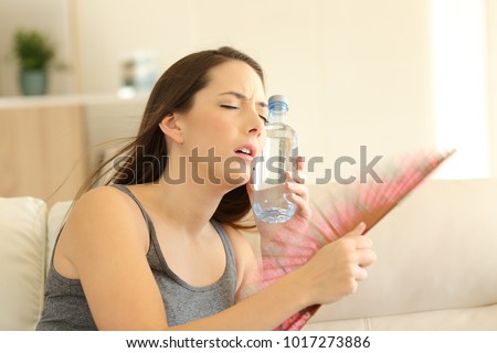 Stressed girl suffering a heatstroke refreshing with a fan sitting on a couch in the living room at home Royalty-Free Stock Photo #1017273886