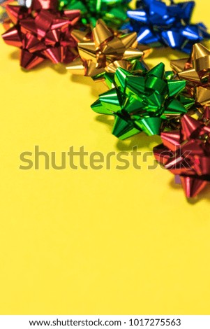 Colorful shiny paper gift bows on bright yellow background, giving or wrapping gifts concept