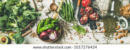 Winter vegetarian, vegan food cooking ingredients. Flat-lay of vegetables, fruit, beans, cereals, kitchen utencil, dried flowers, olive oil over white wooden background, top view. Clean eating food Royalty-Free Stock Photo #1017276424