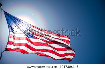 American flag waving in the wind on a perfect nice day with bright sunshine illuminating the flag from behind a clear symbol of freedom and a safe place for immigrants