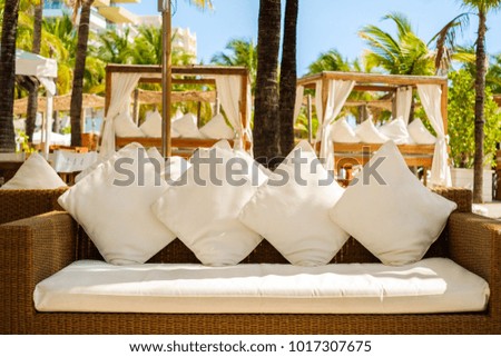 Close up view of an outdoor resort white sofa with palm trees in the background.