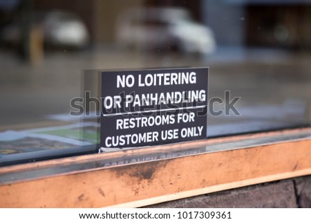 Sign for no loitering or panhandling on the glass window of a store