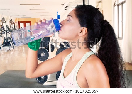 Picture of African woman drinking water after doing a workout while standing in the fitness center
