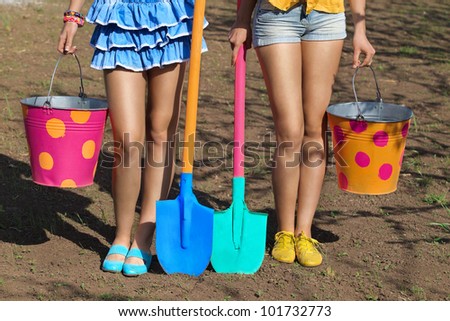 Two pair of female legs with buckets and shovels on garden