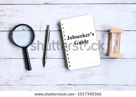 Top view of magnifying glass,hourglass,pen and notebook written with 'JOBSEEKER'S GUIDE' on white wooden background. Royalty-Free Stock Photo #1017340366
