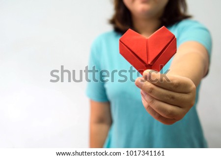An asian woman holding heart origami in front of her chest. A woman giving red heart paper to someone. Love and give concept for valentine day.