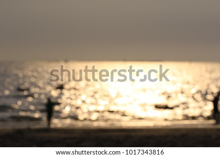 Peoples are playing on the beach at the sunset on blurred background.