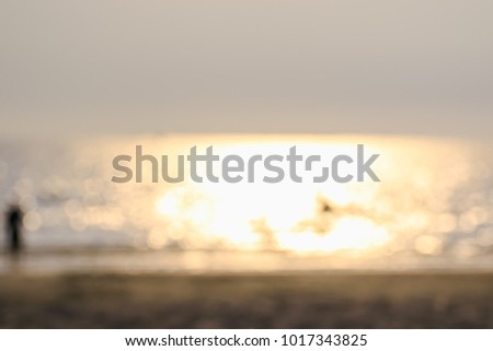 Peoples are playing on the beach at the sunset on blurred background.